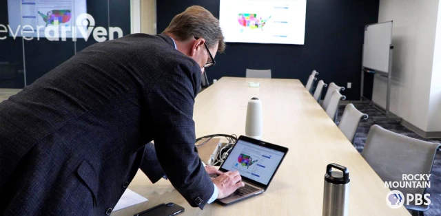 A man in a suit working on his laptop seated in a EverDriven's conference room, engaged in a professional setting.
