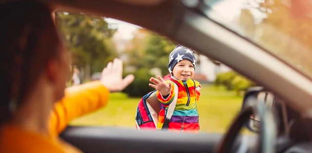A cheerful child waves to the driver from the open window of a car, showcasing a moment of joy.
