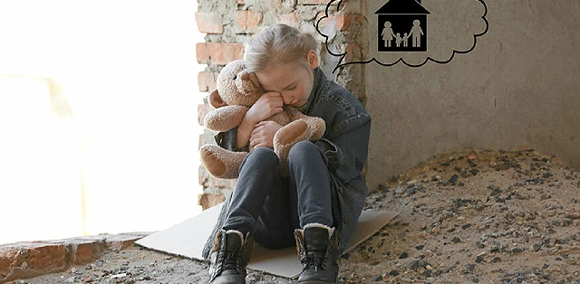 A young girl, appearing sorrowful, sits on the ground with a teddy bear held tightly in her arms.