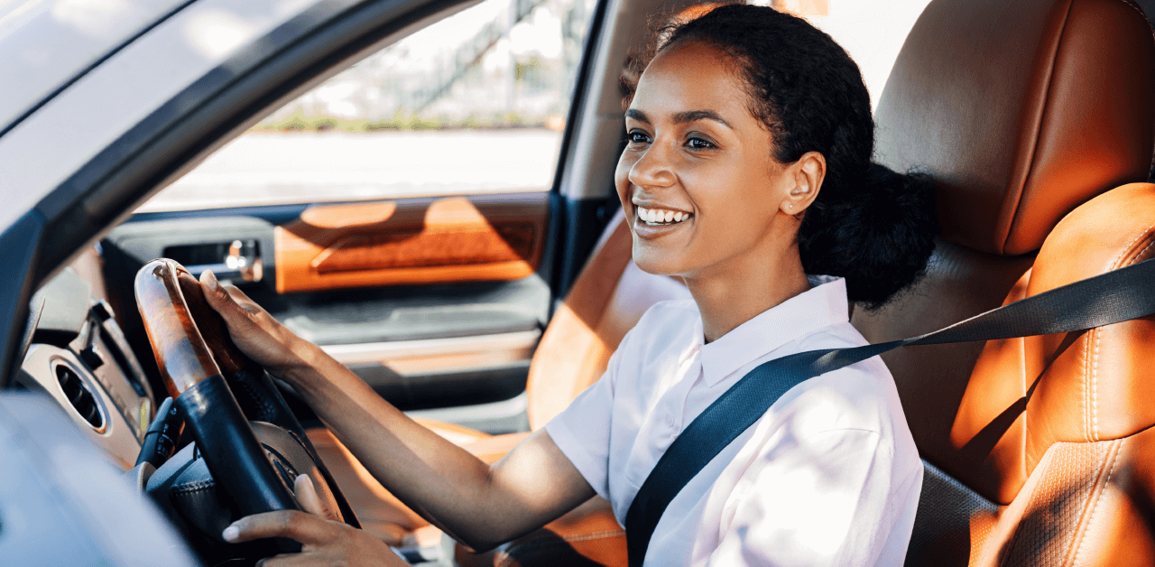 A woman with a bright smile is driving her car, reflecting a positive and carefree attitude while on the road.