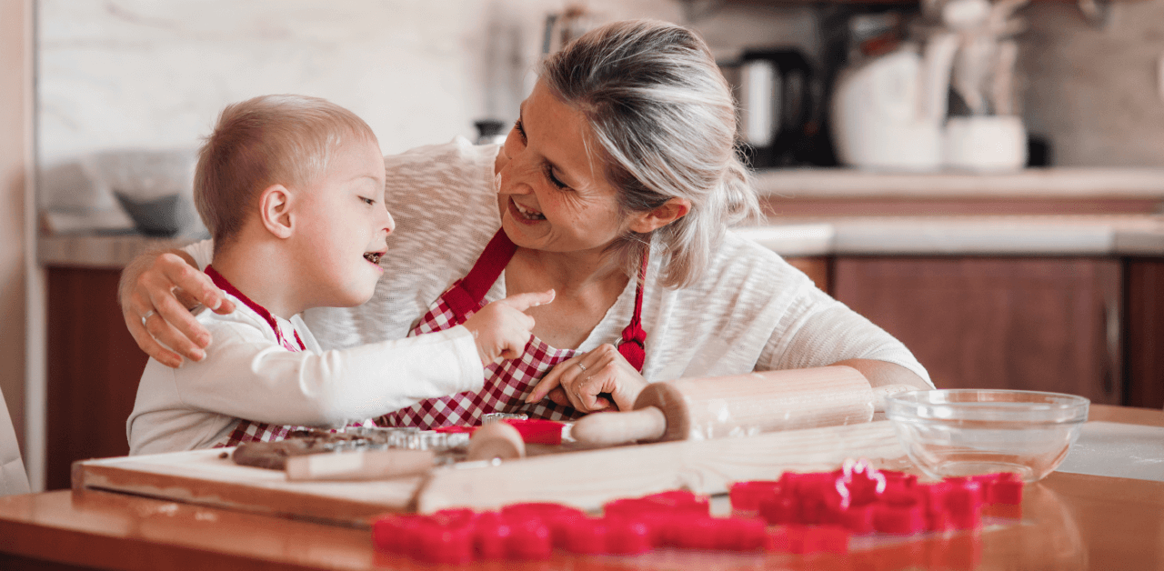 A smiling woman and a child with special in a kitchen setting surrounded by baking supplies.
