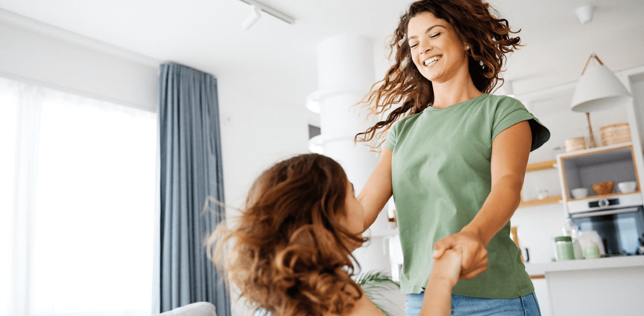 A woman and a little girl joyfully dancing together in a home setting, showcasing a moment of happiness.
