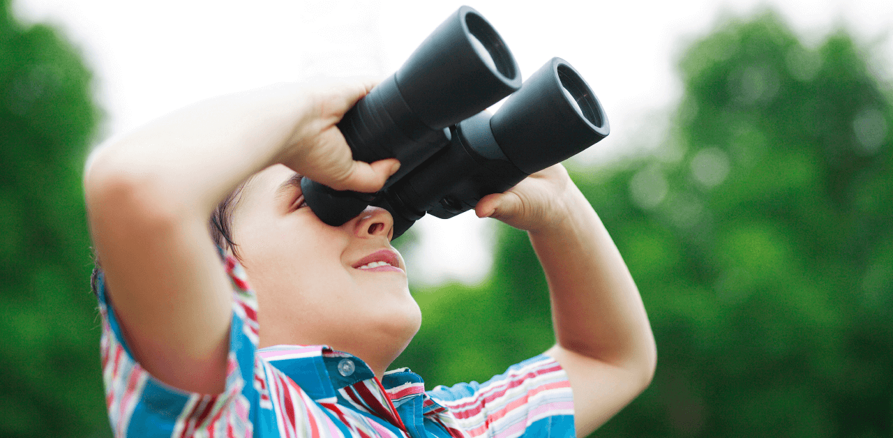 A young boy intently looks through binoculars in an outdoor setting.