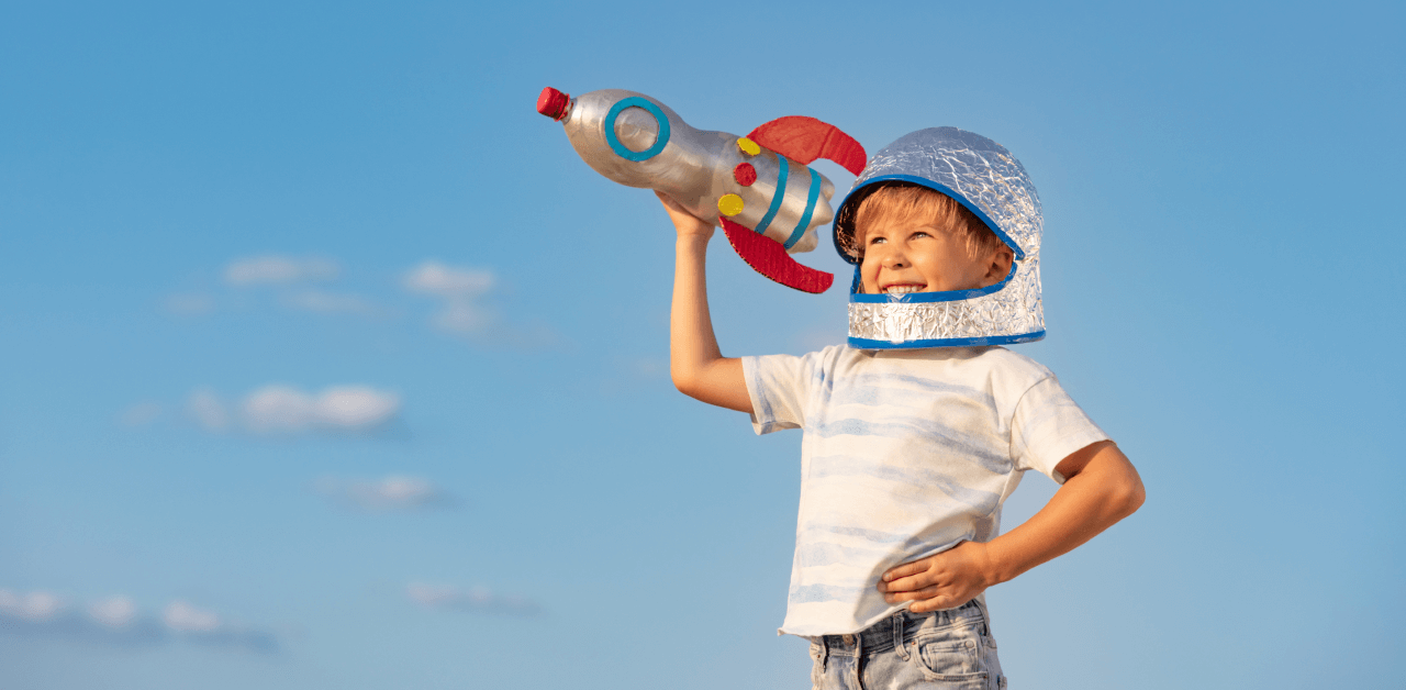 A young boy joyfully holds a colorful toy rocket made out of a plastic bottle.