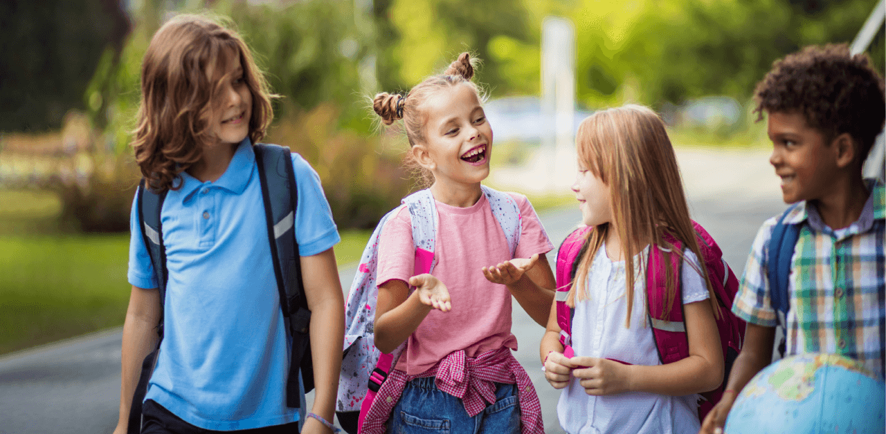 A group of 4 children walking together with backpacks, engaged in cheerful conversation.