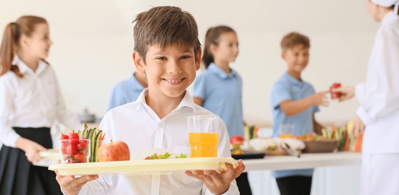 A young boy holding a tray vibrant fruits and vegetables, surrounded by children.