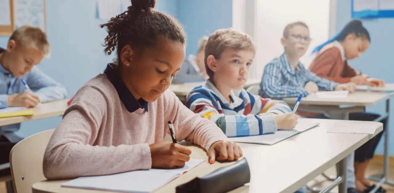 Elementary school students sitting at desks in a classroom, focused on writing in their notebooks during a lesson listening to a lecture and taking notes.
