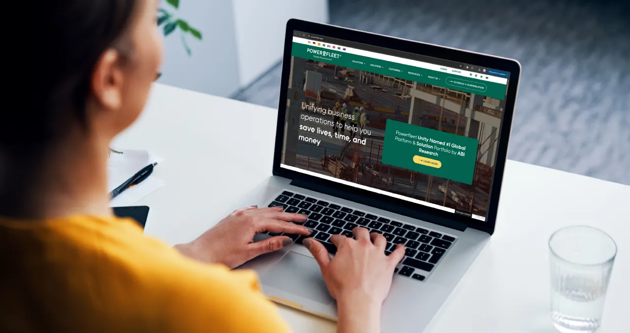 The PowerFleet website displays on a professional’s office laptop. The homepage highlights solutions on unifying business operations.