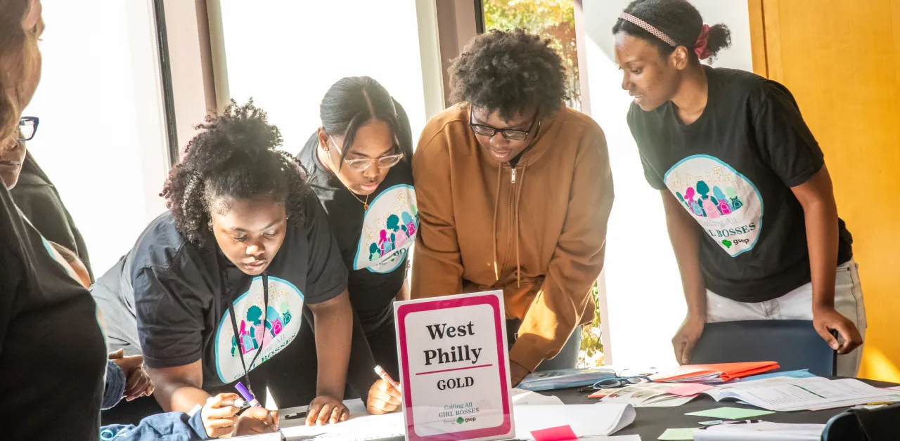 Girl scouts gather around a table with markers and paper materials for a team activity.