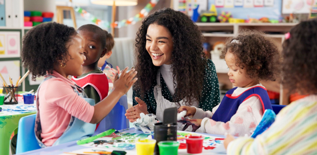 Teacher smiling while engaging with young children during an art activity in a classroom