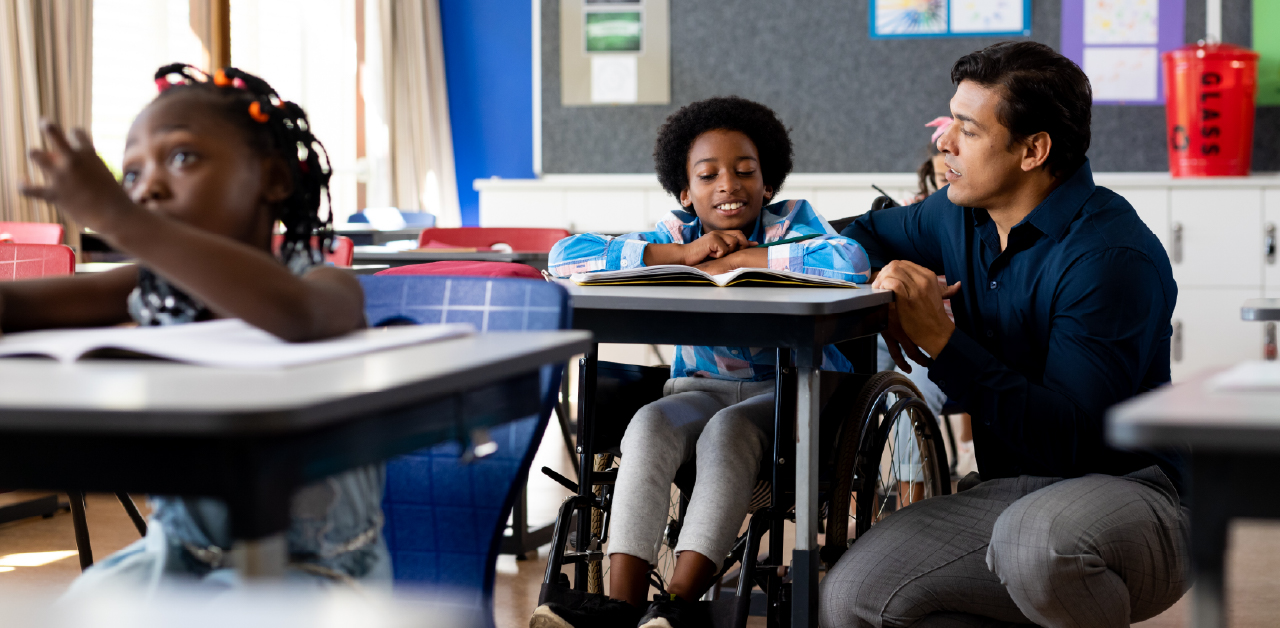 Teacher kneels beside a student in a wheelchair during a classroom lesson