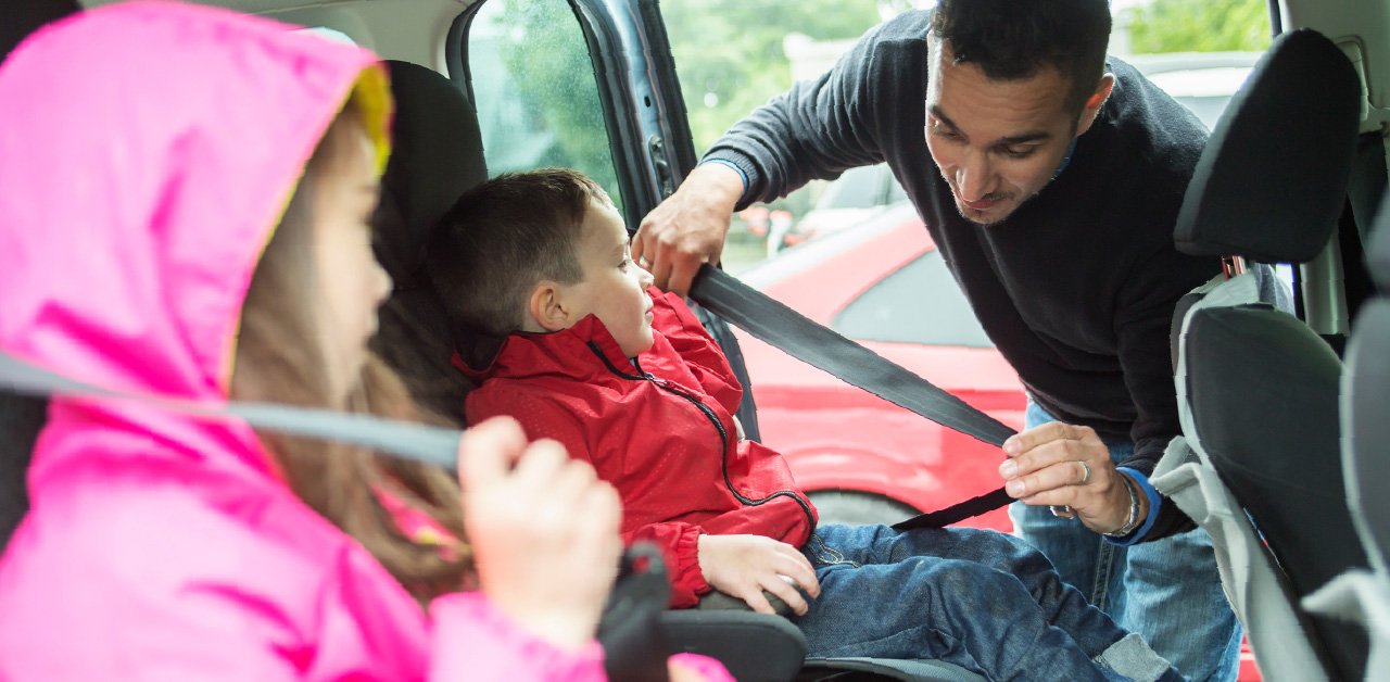 Child seated in a car seat while an adult fastens the seat belt inside a vehicle