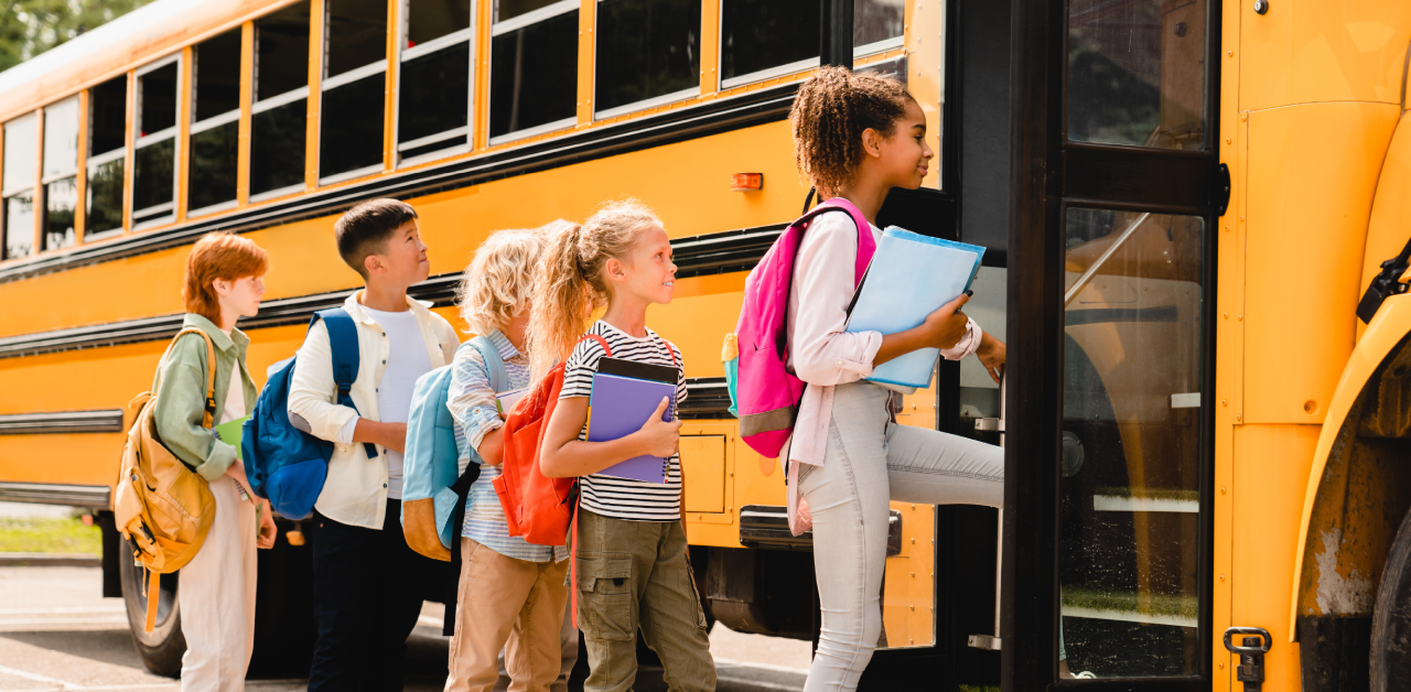 students line up to board a yellow school bus with backpacks and school supplies