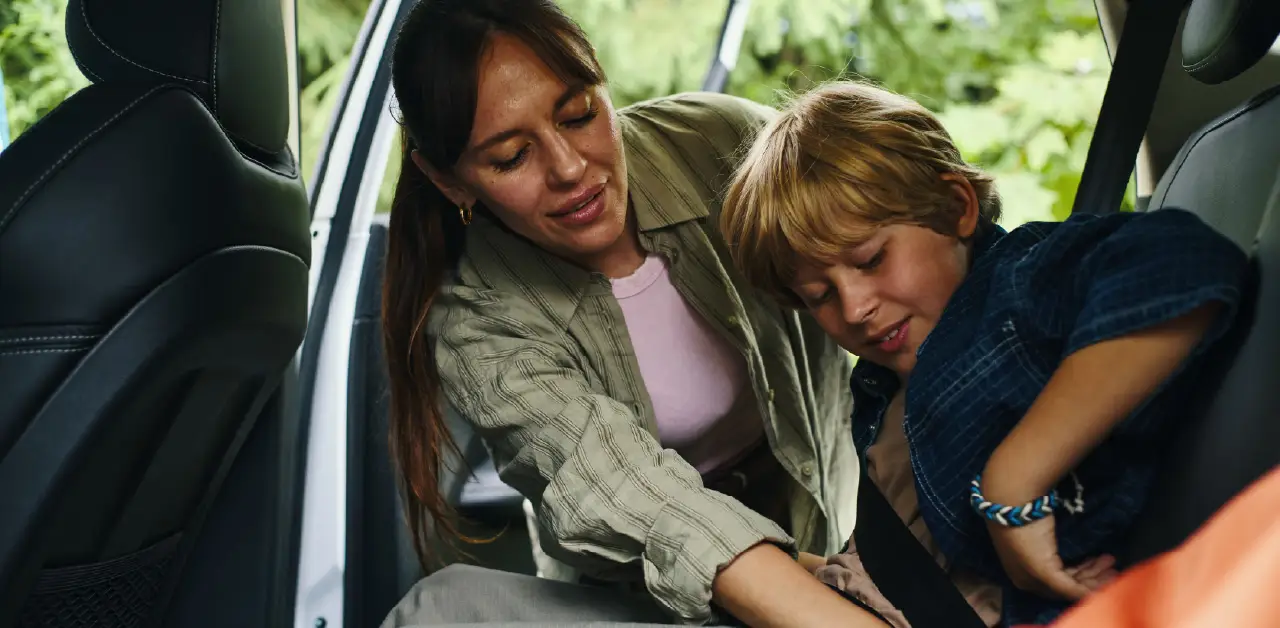 an adult helping a child fasten a seat belt inside a small vehicle