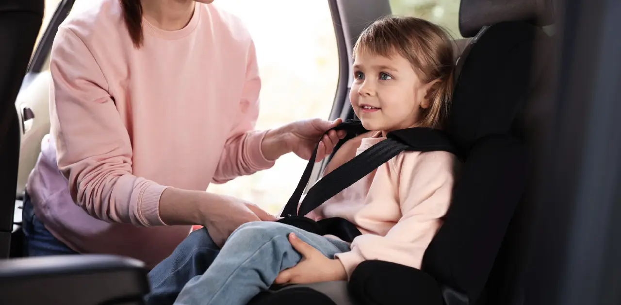 Adult helps a young child secure a car seat inside a small vehicle