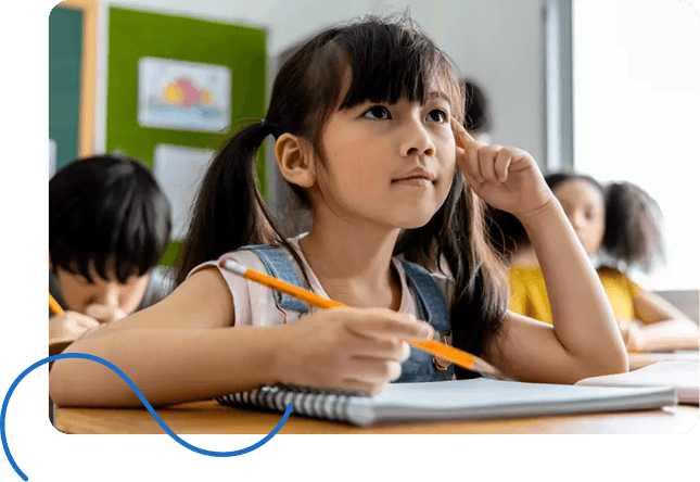 A young girl with a ponytail attentively listens in class, holding a pencil. Behind her, students engage in learning.