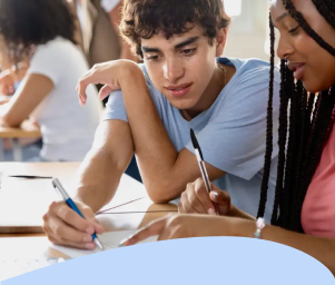 Two students sitting at a desk, collaborating on paperwork. They appear focused and engaged. Text below reads: "Students Experiencing Housing Instability."