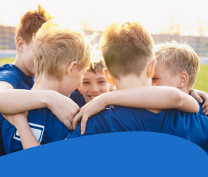 A group of students in blue jerseys huddling together in a field, smiling, conveying teamwork and camaraderie.