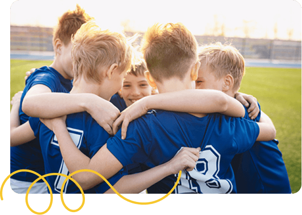 A group of students in blue jerseys huddling together in a field, smiling, conveying teamwork and camaraderie.