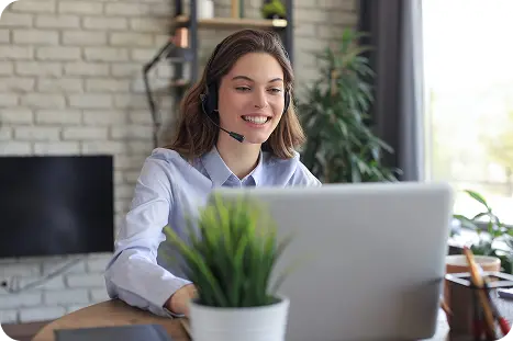 A woman with a headset sits at a desk, focused on her laptop while working.