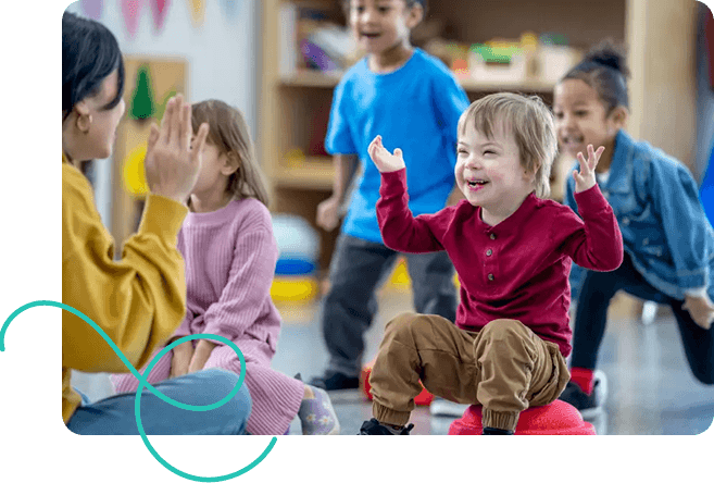 A joyful classroom scene with a young child in a red shirt smiling and raising his hands. He's surrounded by diverse, happy children and a teacher.
