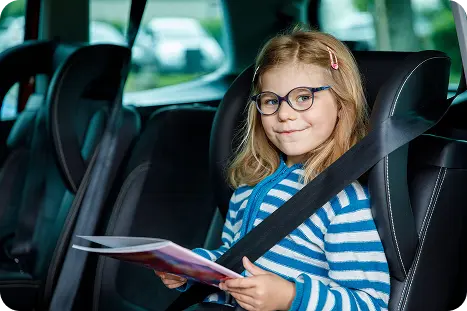 A young girl wearing glasses is seated in the back of a car.