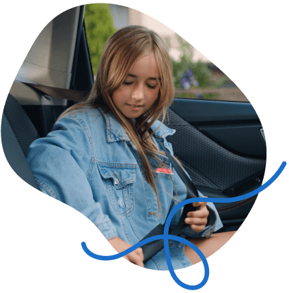 A young girl in a denim jacket sits in a car, buckling her seatbelt with a focused expression.