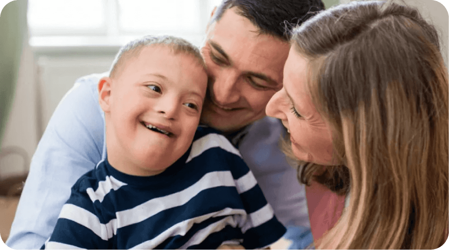 A smiling boy wearing a striped shirt is embraced by his parents.