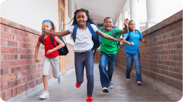 Four joyful children with backpacks run down a school hallway.